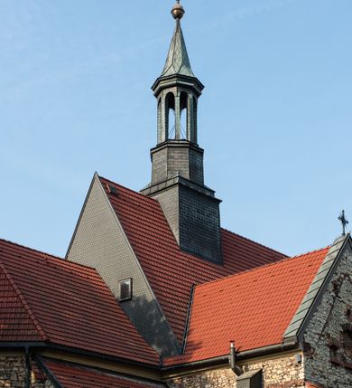 Zdjęcie nr 8: Kościół murowany, orientowany, jednonawowy, trójprzęsłowy, z transeptem i jednoprzęsłowym, węższym i niższym prezbiterium zamkniętym trójbocznie. Między nawą a transeptem po obu stronach znajdują się kruchty, do prezbiterium od strony północnej dostawiona kruchta złożona z dwóch lokalności. Ściany są rozczłonkowane filarami, tworzącymi płytkie arkadowe wnęki. Między nawą a prezbiterium arkada tęczowa. Sklepienie krzyżowe na gurtach spływających na filary. Prezbiterium oświetlają wąskie, prostokątne okna zamknięte ostrołukowo, w nawie i w transepcie znajdują się prostokątne okna prostokątne zamknięte półkoliście, w ścianie frontowej w dolnej części okna prostokątne zamknięte półkoliście, a w górnej podwójne okna prostokątne. Fasada ujęta dwiema narożnymi szkarpami, zwieńczona trójkątnie. Do niej dostawiona kruchta z dwuspadowym daszkiem i wejściem w kształcie prostokąta zamkniętego półkoliście. W kamiennej fasadzie znajdują się dołem okna prostokątne, zamknięte półkoliście, a górą  prostokątne, biforialne okna z nadprożem łukowatym wykonanym z cegły. Szczyt ceglany, podzielony na trzy strefy kamiennym wątkiem, z pięcioma wnękami prostokątnymi, zamkniętymi półkoliście, z wąskimi otworami w dolnej strefie i z owalnym oknem w drugiej. Elewacje boczne nawy ujęte skarpami. Dachy dwuspadowe, kryte dachówką, z wieżyczką na sygnaturkę.         