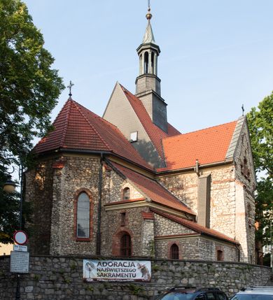 Zdjęcie nr 10: Kościół murowany, orientowany, jednonawowy, trójprzęsłowy, z transeptem i jednoprzęsłowym, węższym i niższym prezbiterium zamkniętym trójbocznie. Między nawą a transeptem po obu stronach znajdują się kruchty, do prezbiterium od strony północnej dostawiona kruchta złożona z dwóch lokalności. Ściany są rozczłonkowane filarami, tworzącymi płytkie arkadowe wnęki. Między nawą a prezbiterium arkada tęczowa. Sklepienie krzyżowe na gurtach spływających na filary. Prezbiterium oświetlają wąskie, prostokątne okna zamknięte ostrołukowo, w nawie i w transepcie znajdują się prostokątne okna prostokątne zamknięte półkoliście, w ścianie frontowej w dolnej części okna prostokątne zamknięte półkoliście, a w górnej podwójne okna prostokątne. Fasada ujęta dwiema narożnymi szkarpami, zwieńczona trójkątnie. Do niej dostawiona kruchta z dwuspadowym daszkiem i wejściem w kształcie prostokąta zamkniętego półkoliście. W kamiennej fasadzie znajdują się dołem okna prostokątne, zamknięte półkoliście, a górą  prostokątne, biforialne okna z nadprożem łukowatym wykonanym z cegły. Szczyt ceglany, podzielony na trzy strefy kamiennym wątkiem, z pięcioma wnękami prostokątnymi, zamkniętymi półkoliście, z wąskimi otworami w dolnej strefie i z owalnym oknem w drugiej. Elewacje boczne nawy ujęte skarpami. Dachy dwuspadowe, kryte dachówką, z wieżyczką na sygnaturkę.         