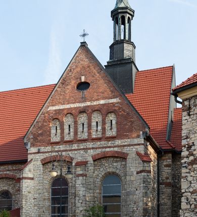 Zdjęcie nr 64: Kościół murowany, orientowany, jednonawowy, trójprzęsłowy, z transeptem i jednoprzęsłowym, węższym i niższym prezbiterium zamkniętym trójbocznie. Między nawą a transeptem po obu stronach znajdują się kruchty, do prezbiterium od strony północnej dostawiona kruchta złożona z dwóch lokalności. Ściany są rozczłonkowane filarami, tworzącymi płytkie arkadowe wnęki. Między nawą a prezbiterium arkada tęczowa. Sklepienie krzyżowe na gurtach spływających na filary. Prezbiterium oświetlają wąskie, prostokątne okna zamknięte ostrołukowo, w nawie i w transepcie znajdują się prostokątne okna prostokątne zamknięte półkoliście, w ścianie frontowej w dolnej części okna prostokątne zamknięte półkoliście, a w górnej podwójne okna prostokątne. Fasada ujęta dwiema narożnymi szkarpami, zwieńczona trójkątnie. Do niej dostawiona kruchta z dwuspadowym daszkiem i wejściem w kształcie prostokąta zamkniętego półkoliście. W kamiennej fasadzie znajdują się dołem okna prostokątne, zamknięte półkoliście, a górą  prostokątne, biforialne okna z nadprożem łukowatym wykonanym z cegły. Szczyt ceglany, podzielony na trzy strefy kamiennym wątkiem, z pięcioma wnękami prostokątnymi, zamkniętymi półkoliście, z wąskimi otworami w dolnej strefie i z owalnym oknem w drugiej. Elewacje boczne nawy ujęte skarpami. Dachy dwuspadowe, kryte dachówką, z wieżyczką na sygnaturkę.         