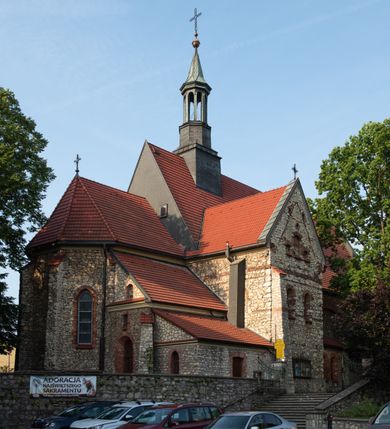 Zdjęcie nr 11: Kościół murowany, orientowany, jednonawowy, trójprzęsłowy, z transeptem i jednoprzęsłowym, węższym i niższym prezbiterium zamkniętym trójbocznie. Między nawą a transeptem po obu stronach znajdują się kruchty, do prezbiterium od strony północnej dostawiona kruchta złożona z dwóch lokalności. Ściany są rozczłonkowane filarami, tworzącymi płytkie arkadowe wnęki. Między nawą a prezbiterium arkada tęczowa. Sklepienie krzyżowe na gurtach spływających na filary. Prezbiterium oświetlają wąskie, prostokątne okna zamknięte ostrołukowo, w nawie i w transepcie znajdują się prostokątne okna prostokątne zamknięte półkoliście, w ścianie frontowej w dolnej części okna prostokątne zamknięte półkoliście, a w górnej podwójne okna prostokątne. Fasada ujęta dwiema narożnymi szkarpami, zwieńczona trójkątnie. Do niej dostawiona kruchta z dwuspadowym daszkiem i wejściem w kształcie prostokąta zamkniętego półkoliście. W kamiennej fasadzie znajdują się dołem okna prostokątne, zamknięte półkoliście, a górą  prostokątne, biforialne okna z nadprożem łukowatym wykonanym z cegły. Szczyt ceglany, podzielony na trzy strefy kamiennym wątkiem, z pięcioma wnękami prostokątnymi, zamkniętymi półkoliście, z wąskimi otworami w dolnej strefie i z owalnym oknem w drugiej. Elewacje boczne nawy ujęte skarpami. Dachy dwuspadowe, kryte dachówką, z wieżyczką na sygnaturkę.         