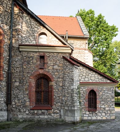 Zdjęcie nr 14: Kościół murowany, orientowany, jednonawowy, trójprzęsłowy, z transeptem i jednoprzęsłowym, węższym i niższym prezbiterium zamkniętym trójbocznie. Między nawą a transeptem po obu stronach znajdują się kruchty, do prezbiterium od strony północnej dostawiona kruchta złożona z dwóch lokalności. Ściany są rozczłonkowane filarami, tworzącymi płytkie arkadowe wnęki. Między nawą a prezbiterium arkada tęczowa. Sklepienie krzyżowe na gurtach spływających na filary. Prezbiterium oświetlają wąskie, prostokątne okna zamknięte ostrołukowo, w nawie i w transepcie znajdują się prostokątne okna prostokątne zamknięte półkoliście, w ścianie frontowej w dolnej części okna prostokątne zamknięte półkoliście, a w górnej podwójne okna prostokątne. Fasada ujęta dwiema narożnymi szkarpami, zwieńczona trójkątnie. Do niej dostawiona kruchta z dwuspadowym daszkiem i wejściem w kształcie prostokąta zamkniętego półkoliście. W kamiennej fasadzie znajdują się dołem okna prostokątne, zamknięte półkoliście, a górą  prostokątne, biforialne okna z nadprożem łukowatym wykonanym z cegły. Szczyt ceglany, podzielony na trzy strefy kamiennym wątkiem, z pięcioma wnękami prostokątnymi, zamkniętymi półkoliście, z wąskimi otworami w dolnej strefie i z owalnym oknem w drugiej. Elewacje boczne nawy ujęte skarpami. Dachy dwuspadowe, kryte dachówką, z wieżyczką na sygnaturkę.         