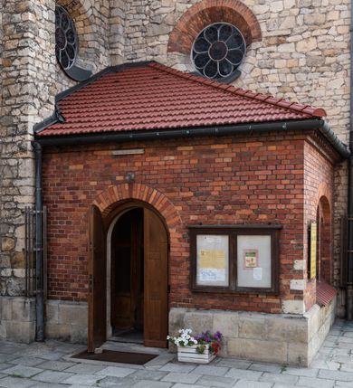 Zdjęcie nr 19: Kościół murowany, orientowany, jednonawowy, trójprzęsłowy, z transeptem i jednoprzęsłowym, węższym i niższym prezbiterium zamkniętym trójbocznie. Między nawą a transeptem po obu stronach znajdują się kruchty, do prezbiterium od strony północnej dostawiona kruchta złożona z dwóch lokalności. Ściany są rozczłonkowane filarami, tworzącymi płytkie arkadowe wnęki. Między nawą a prezbiterium arkada tęczowa. Sklepienie krzyżowe na gurtach spływających na filary. Prezbiterium oświetlają wąskie, prostokątne okna zamknięte ostrołukowo, w nawie i w transepcie znajdują się prostokątne okna prostokątne zamknięte półkoliście, w ścianie frontowej w dolnej części okna prostokątne zamknięte półkoliście, a w górnej podwójne okna prostokątne. Fasada ujęta dwiema narożnymi szkarpami, zwieńczona trójkątnie. Do niej dostawiona kruchta z dwuspadowym daszkiem i wejściem w kształcie prostokąta zamkniętego półkoliście. W kamiennej fasadzie znajdują się dołem okna prostokątne, zamknięte półkoliście, a górą  prostokątne, biforialne okna z nadprożem łukowatym wykonanym z cegły. Szczyt ceglany, podzielony na trzy strefy kamiennym wątkiem, z pięcioma wnękami prostokątnymi, zamkniętymi półkoliście, z wąskimi otworami w dolnej strefie i z owalnym oknem w drugiej. Elewacje boczne nawy ujęte skarpami. Dachy dwuspadowe, kryte dachówką, z wieżyczką na sygnaturkę.         