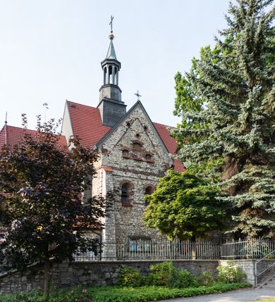 Zdjęcie nr 23: Kościół murowany, orientowany, jednonawowy, trójprzęsłowy, z transeptem i jednoprzęsłowym, węższym i niższym prezbiterium zamkniętym trójbocznie. Między nawą a transeptem po obu stronach znajdują się kruchty, do prezbiterium od strony północnej dostawiona kruchta złożona z dwóch lokalności. Ściany są rozczłonkowane filarami, tworzącymi płytkie arkadowe wnęki. Między nawą a prezbiterium arkada tęczowa. Sklepienie krzyżowe na gurtach spływających na filary. Prezbiterium oświetlają wąskie, prostokątne okna zamknięte ostrołukowo, w nawie i w transepcie znajdują się prostokątne okna prostokątne zamknięte półkoliście, w ścianie frontowej w dolnej części okna prostokątne zamknięte półkoliście, a w górnej podwójne okna prostokątne. Fasada ujęta dwiema narożnymi szkarpami, zwieńczona trójkątnie. Do niej dostawiona kruchta z dwuspadowym daszkiem i wejściem w kształcie prostokąta zamkniętego półkoliście. W kamiennej fasadzie znajdują się dołem okna prostokątne, zamknięte półkoliście, a górą  prostokątne, biforialne okna z nadprożem łukowatym wykonanym z cegły. Szczyt ceglany, podzielony na trzy strefy kamiennym wątkiem, z pięcioma wnękami prostokątnymi, zamkniętymi półkoliście, z wąskimi otworami w dolnej strefie i z owalnym oknem w drugiej. Elewacje boczne nawy ujęte skarpami. Dachy dwuspadowe, kryte dachówką, z wieżyczką na sygnaturkę.         