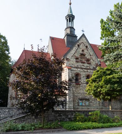 Zdjęcie nr 25: Kościół murowany, orientowany, jednonawowy, trójprzęsłowy, z transeptem i jednoprzęsłowym, węższym i niższym prezbiterium zamkniętym trójbocznie. Między nawą a transeptem po obu stronach znajdują się kruchty, do prezbiterium od strony północnej dostawiona kruchta złożona z dwóch lokalności. Ściany są rozczłonkowane filarami, tworzącymi płytkie arkadowe wnęki. Między nawą a prezbiterium arkada tęczowa. Sklepienie krzyżowe na gurtach spływających na filary. Prezbiterium oświetlają wąskie, prostokątne okna zamknięte ostrołukowo, w nawie i w transepcie znajdują się prostokątne okna prostokątne zamknięte półkoliście, w ścianie frontowej w dolnej części okna prostokątne zamknięte półkoliście, a w górnej podwójne okna prostokątne. Fasada ujęta dwiema narożnymi szkarpami, zwieńczona trójkątnie. Do niej dostawiona kruchta z dwuspadowym daszkiem i wejściem w kształcie prostokąta zamkniętego półkoliście. W kamiennej fasadzie znajdują się dołem okna prostokątne, zamknięte półkoliście, a górą  prostokątne, biforialne okna z nadprożem łukowatym wykonanym z cegły. Szczyt ceglany, podzielony na trzy strefy kamiennym wątkiem, z pięcioma wnękami prostokątnymi, zamkniętymi półkoliście, z wąskimi otworami w dolnej strefie i z owalnym oknem w drugiej. Elewacje boczne nawy ujęte skarpami. Dachy dwuspadowe, kryte dachówką, z wieżyczką na sygnaturkę.         