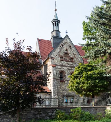 Zdjęcie nr 26: Kościół murowany, orientowany, jednonawowy, trójprzęsłowy, z transeptem i jednoprzęsłowym, węższym i niższym prezbiterium zamkniętym trójbocznie. Między nawą a transeptem po obu stronach znajdują się kruchty, do prezbiterium od strony północnej dostawiona kruchta złożona z dwóch lokalności. Ściany są rozczłonkowane filarami, tworzącymi płytkie arkadowe wnęki. Między nawą a prezbiterium arkada tęczowa. Sklepienie krzyżowe na gurtach spływających na filary. Prezbiterium oświetlają wąskie, prostokątne okna zamknięte ostrołukowo, w nawie i w transepcie znajdują się prostokątne okna prostokątne zamknięte półkoliście, w ścianie frontowej w dolnej części okna prostokątne zamknięte półkoliście, a w górnej podwójne okna prostokątne. Fasada ujęta dwiema narożnymi szkarpami, zwieńczona trójkątnie. Do niej dostawiona kruchta z dwuspadowym daszkiem i wejściem w kształcie prostokąta zamkniętego półkoliście. W kamiennej fasadzie znajdują się dołem okna prostokątne, zamknięte półkoliście, a górą  prostokątne, biforialne okna z nadprożem łukowatym wykonanym z cegły. Szczyt ceglany, podzielony na trzy strefy kamiennym wątkiem, z pięcioma wnękami prostokątnymi, zamkniętymi półkoliście, z wąskimi otworami w dolnej strefie i z owalnym oknem w drugiej. Elewacje boczne nawy ujęte skarpami. Dachy dwuspadowe, kryte dachówką, z wieżyczką na sygnaturkę.         