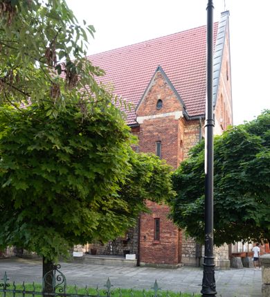Zdjęcie nr 27: Kościół murowany, orientowany, jednonawowy, trójprzęsłowy, z transeptem i jednoprzęsłowym, węższym i niższym prezbiterium zamkniętym trójbocznie. Między nawą a transeptem po obu stronach znajdują się kruchty, do prezbiterium od strony północnej dostawiona kruchta złożona z dwóch lokalności. Ściany są rozczłonkowane filarami, tworzącymi płytkie arkadowe wnęki. Między nawą a prezbiterium arkada tęczowa. Sklepienie krzyżowe na gurtach spływających na filary. Prezbiterium oświetlają wąskie, prostokątne okna zamknięte ostrołukowo, w nawie i w transepcie znajdują się prostokątne okna prostokątne zamknięte półkoliście, w ścianie frontowej w dolnej części okna prostokątne zamknięte półkoliście, a w górnej podwójne okna prostokątne. Fasada ujęta dwiema narożnymi szkarpami, zwieńczona trójkątnie. Do niej dostawiona kruchta z dwuspadowym daszkiem i wejściem w kształcie prostokąta zamkniętego półkoliście. W kamiennej fasadzie znajdują się dołem okna prostokątne, zamknięte półkoliście, a górą  prostokątne, biforialne okna z nadprożem łukowatym wykonanym z cegły. Szczyt ceglany, podzielony na trzy strefy kamiennym wątkiem, z pięcioma wnękami prostokątnymi, zamkniętymi półkoliście, z wąskimi otworami w dolnej strefie i z owalnym oknem w drugiej. Elewacje boczne nawy ujęte skarpami. Dachy dwuspadowe, kryte dachówką, z wieżyczką na sygnaturkę.         