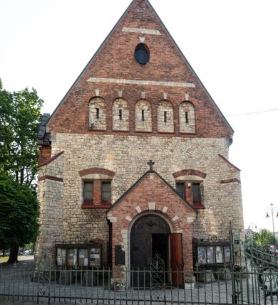 Zdjęcie nr 35: Kościół murowany, orientowany, jednonawowy, trójprzęsłowy, z transeptem i jednoprzęsłowym, węższym i niższym prezbiterium zamkniętym trójbocznie. Między nawą a transeptem po obu stronach znajdują się kruchty, do prezbiterium od strony północnej dostawiona kruchta złożona z dwóch lokalności. Ściany są rozczłonkowane filarami, tworzącymi płytkie arkadowe wnęki. Między nawą a prezbiterium arkada tęczowa. Sklepienie krzyżowe na gurtach spływających na filary. Prezbiterium oświetlają wąskie, prostokątne okna zamknięte ostrołukowo, w nawie i w transepcie znajdują się prostokątne okna prostokątne zamknięte półkoliście, w ścianie frontowej w dolnej części okna prostokątne zamknięte półkoliście, a w górnej podwójne okna prostokątne. Fasada ujęta dwiema narożnymi szkarpami, zwieńczona trójkątnie. Do niej dostawiona kruchta z dwuspadowym daszkiem i wejściem w kształcie prostokąta zamkniętego półkoliście. W kamiennej fasadzie znajdują się dołem okna prostokątne, zamknięte półkoliście, a górą  prostokątne, biforialne okna z nadprożem łukowatym wykonanym z cegły. Szczyt ceglany, podzielony na trzy strefy kamiennym wątkiem, z pięcioma wnękami prostokątnymi, zamkniętymi półkoliście, z wąskimi otworami w dolnej strefie i z owalnym oknem w drugiej. Elewacje boczne nawy ujęte skarpami. Dachy dwuspadowe, kryte dachówką, z wieżyczką na sygnaturkę.         