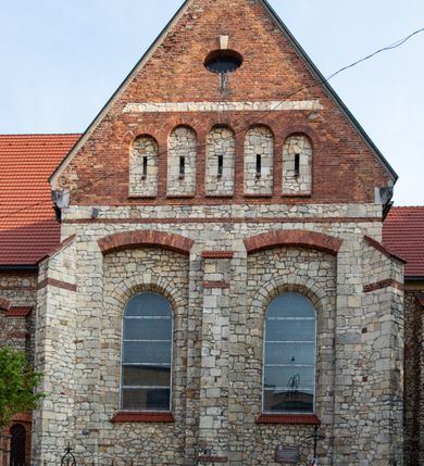 Zdjęcie nr 30: Kościół murowany, orientowany, jednonawowy, trójprzęsłowy, z transeptem i jednoprzęsłowym, węższym i niższym prezbiterium zamkniętym trójbocznie. Między nawą a transeptem po obu stronach znajdują się kruchty, do prezbiterium od strony północnej dostawiona kruchta złożona z dwóch lokalności. Ściany są rozczłonkowane filarami, tworzącymi płytkie arkadowe wnęki. Między nawą a prezbiterium arkada tęczowa. Sklepienie krzyżowe na gurtach spływających na filary. Prezbiterium oświetlają wąskie, prostokątne okna zamknięte ostrołukowo, w nawie i w transepcie znajdują się prostokątne okna prostokątne zamknięte półkoliście, w ścianie frontowej w dolnej części okna prostokątne zamknięte półkoliście, a w górnej podwójne okna prostokątne. Fasada ujęta dwiema narożnymi szkarpami, zwieńczona trójkątnie. Do niej dostawiona kruchta z dwuspadowym daszkiem i wejściem w kształcie prostokąta zamkniętego półkoliście. W kamiennej fasadzie znajdują się dołem okna prostokątne, zamknięte półkoliście, a górą  prostokątne, biforialne okna z nadprożem łukowatym wykonanym z cegły. Szczyt ceglany, podzielony na trzy strefy kamiennym wątkiem, z pięcioma wnękami prostokątnymi, zamkniętymi półkoliście, z wąskimi otworami w dolnej strefie i z owalnym oknem w drugiej. Elewacje boczne nawy ujęte skarpami. Dachy dwuspadowe, kryte dachówką, z wieżyczką na sygnaturkę.         