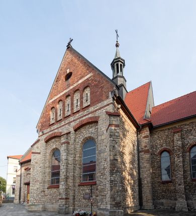 Zdjęcie nr 31: Kościół murowany, orientowany, jednonawowy, trójprzęsłowy, z transeptem i jednoprzęsłowym, węższym i niższym prezbiterium zamkniętym trójbocznie. Między nawą a transeptem po obu stronach znajdują się kruchty, do prezbiterium od strony północnej dostawiona kruchta złożona z dwóch lokalności. Ściany są rozczłonkowane filarami, tworzącymi płytkie arkadowe wnęki. Między nawą a prezbiterium arkada tęczowa. Sklepienie krzyżowe na gurtach spływających na filary. Prezbiterium oświetlają wąskie, prostokątne okna zamknięte ostrołukowo, w nawie i w transepcie znajdują się prostokątne okna prostokątne zamknięte półkoliście, w ścianie frontowej w dolnej części okna prostokątne zamknięte półkoliście, a w górnej podwójne okna prostokątne. Fasada ujęta dwiema narożnymi szkarpami, zwieńczona trójkątnie. Do niej dostawiona kruchta z dwuspadowym daszkiem i wejściem w kształcie prostokąta zamkniętego półkoliście. W kamiennej fasadzie znajdują się dołem okna prostokątne, zamknięte półkoliście, a górą  prostokątne, biforialne okna z nadprożem łukowatym wykonanym z cegły. Szczyt ceglany, podzielony na trzy strefy kamiennym wątkiem, z pięcioma wnękami prostokątnymi, zamkniętymi półkoliście, z wąskimi otworami w dolnej strefie i z owalnym oknem w drugiej. Elewacje boczne nawy ujęte skarpami. Dachy dwuspadowe, kryte dachówką, z wieżyczką na sygnaturkę.         