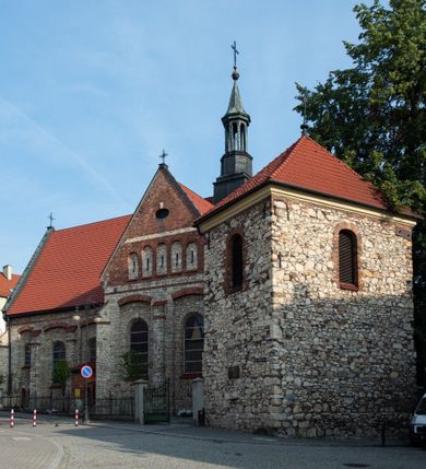 Zdjęcie nr 29: Kościół murowany, orientowany, jednonawowy, trójprzęsłowy, z transeptem i jednoprzęsłowym, węższym i niższym prezbiterium zamkniętym trójbocznie. Między nawą a transeptem po obu stronach znajdują się kruchty, do prezbiterium od strony północnej dostawiona kruchta złożona z dwóch lokalności. Ściany są rozczłonkowane filarami, tworzącymi płytkie arkadowe wnęki. Między nawą a prezbiterium arkada tęczowa. Sklepienie krzyżowe na gurtach spływających na filary. Prezbiterium oświetlają wąskie, prostokątne okna zamknięte ostrołukowo, w nawie i w transepcie znajdują się prostokątne okna prostokątne zamknięte półkoliście, w ścianie frontowej w dolnej części okna prostokątne zamknięte półkoliście, a w górnej podwójne okna prostokątne. Fasada ujęta dwiema narożnymi szkarpami, zwieńczona trójkątnie. Do niej dostawiona kruchta z dwuspadowym daszkiem i wejściem w kształcie prostokąta zamkniętego półkoliście. W kamiennej fasadzie znajdują się dołem okna prostokątne, zamknięte półkoliście, a górą  prostokątne, biforialne okna z nadprożem łukowatym wykonanym z cegły. Szczyt ceglany, podzielony na trzy strefy kamiennym wątkiem, z pięcioma wnękami prostokątnymi, zamkniętymi półkoliście, z wąskimi otworami w dolnej strefie i z owalnym oknem w drugiej. Elewacje boczne nawy ujęte skarpami. Dachy dwuspadowe, kryte dachówką, z wieżyczką na sygnaturkę.         