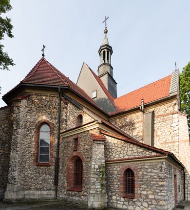 Zdjęcie nr 34: Kościół murowany, orientowany, jednonawowy, trójprzęsłowy, z transeptem i jednoprzęsłowym, węższym i niższym prezbiterium zamkniętym trójbocznie. Między nawą a transeptem po obu stronach znajdują się kruchty, do prezbiterium od strony północnej dostawiona kruchta złożona z dwóch lokalności. Ściany są rozczłonkowane filarami, tworzącymi płytkie arkadowe wnęki. Między nawą a prezbiterium arkada tęczowa. Sklepienie krzyżowe na gurtach spływających na filary. Prezbiterium oświetlają wąskie, prostokątne okna zamknięte ostrołukowo, w nawie i w transepcie znajdują się prostokątne okna prostokątne zamknięte półkoliście, w ścianie frontowej w dolnej części okna prostokątne zamknięte półkoliście, a w górnej podwójne okna prostokątne. Fasada ujęta dwiema narożnymi szkarpami, zwieńczona trójkątnie. Do niej dostawiona kruchta z dwuspadowym daszkiem i wejściem w kształcie prostokąta zamkniętego półkoliście. W kamiennej fasadzie znajdują się dołem okna prostokątne, zamknięte półkoliście, a górą  prostokątne, biforialne okna z nadprożem łukowatym wykonanym z cegły. Szczyt ceglany, podzielony na trzy strefy kamiennym wątkiem, z pięcioma wnękami prostokątnymi, zamkniętymi półkoliście, z wąskimi otworami w dolnej strefie i z owalnym oknem w drugiej. Elewacje boczne nawy ujęte skarpami. Dachy dwuspadowe, kryte dachówką, z wieżyczką na sygnaturkę.         