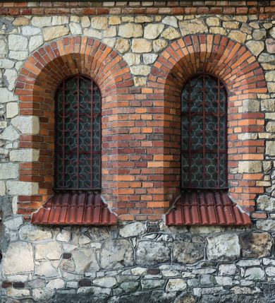 Zdjęcie nr 44: Kościół murowany, orientowany, jednonawowy, trójprzęsłowy, z transeptem i jednoprzęsłowym, węższym i niższym prezbiterium zamkniętym trójbocznie. Między nawą a transeptem po obu stronach znajdują się kruchty, do prezbiterium od strony północnej dostawiona kruchta złożona z dwóch lokalności. Ściany są rozczłonkowane filarami, tworzącymi płytkie arkadowe wnęki. Między nawą a prezbiterium arkada tęczowa. Sklepienie krzyżowe na gurtach spływających na filary. Prezbiterium oświetlają wąskie, prostokątne okna zamknięte ostrołukowo, w nawie i w transepcie znajdują się prostokątne okna prostokątne zamknięte półkoliście, w ścianie frontowej w dolnej części okna prostokątne zamknięte półkoliście, a w górnej podwójne okna prostokątne. Fasada ujęta dwiema narożnymi szkarpami, zwieńczona trójkątnie. Do niej dostawiona kruchta z dwuspadowym daszkiem i wejściem w kształcie prostokąta zamkniętego półkoliście. W kamiennej fasadzie znajdują się dołem okna prostokątne, zamknięte półkoliście, a górą  prostokątne, biforialne okna z nadprożem łukowatym wykonanym z cegły. Szczyt ceglany, podzielony na trzy strefy kamiennym wątkiem, z pięcioma wnękami prostokątnymi, zamkniętymi półkoliście, z wąskimi otworami w dolnej strefie i z owalnym oknem w drugiej. Elewacje boczne nawy ujęte skarpami. Dachy dwuspadowe, kryte dachówką, z wieżyczką na sygnaturkę.         