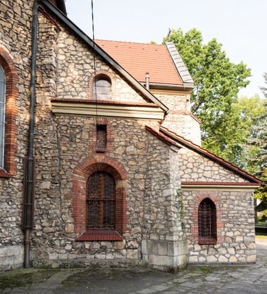 Zdjęcie nr 38: Kościół murowany, orientowany, jednonawowy, trójprzęsłowy, z transeptem i jednoprzęsłowym, węższym i niższym prezbiterium zamkniętym trójbocznie. Między nawą a transeptem po obu stronach znajdują się kruchty, do prezbiterium od strony północnej dostawiona kruchta złożona z dwóch lokalności. Ściany są rozczłonkowane filarami, tworzącymi płytkie arkadowe wnęki. Między nawą a prezbiterium arkada tęczowa. Sklepienie krzyżowe na gurtach spływających na filary. Prezbiterium oświetlają wąskie, prostokątne okna zamknięte ostrołukowo, w nawie i w transepcie znajdują się prostokątne okna prostokątne zamknięte półkoliście, w ścianie frontowej w dolnej części okna prostokątne zamknięte półkoliście, a w górnej podwójne okna prostokątne. Fasada ujęta dwiema narożnymi szkarpami, zwieńczona trójkątnie. Do niej dostawiona kruchta z dwuspadowym daszkiem i wejściem w kształcie prostokąta zamkniętego półkoliście. W kamiennej fasadzie znajdują się dołem okna prostokątne, zamknięte półkoliście, a górą  prostokątne, biforialne okna z nadprożem łukowatym wykonanym z cegły. Szczyt ceglany, podzielony na trzy strefy kamiennym wątkiem, z pięcioma wnękami prostokątnymi, zamkniętymi półkoliście, z wąskimi otworami w dolnej strefie i z owalnym oknem w drugiej. Elewacje boczne nawy ujęte skarpami. Dachy dwuspadowe, kryte dachówką, z wieżyczką na sygnaturkę.         