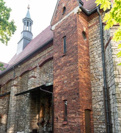 Zdjęcie nr 37: Kościół murowany, orientowany, jednonawowy, trójprzęsłowy, z transeptem i jednoprzęsłowym, węższym i niższym prezbiterium zamkniętym trójbocznie. Między nawą a transeptem po obu stronach znajdują się kruchty, do prezbiterium od strony północnej dostawiona kruchta złożona z dwóch lokalności. Ściany są rozczłonkowane filarami, tworzącymi płytkie arkadowe wnęki. Między nawą a prezbiterium arkada tęczowa. Sklepienie krzyżowe na gurtach spływających na filary. Prezbiterium oświetlają wąskie, prostokątne okna zamknięte ostrołukowo, w nawie i w transepcie znajdują się prostokątne okna prostokątne zamknięte półkoliście, w ścianie frontowej w dolnej części okna prostokątne zamknięte półkoliście, a w górnej podwójne okna prostokątne. Fasada ujęta dwiema narożnymi szkarpami, zwieńczona trójkątnie. Do niej dostawiona kruchta z dwuspadowym daszkiem i wejściem w kształcie prostokąta zamkniętego półkoliście. W kamiennej fasadzie znajdują się dołem okna prostokątne, zamknięte półkoliście, a górą  prostokątne, biforialne okna z nadprożem łukowatym wykonanym z cegły. Szczyt ceglany, podzielony na trzy strefy kamiennym wątkiem, z pięcioma wnękami prostokątnymi, zamkniętymi półkoliście, z wąskimi otworami w dolnej strefie i z owalnym oknem w drugiej. Elewacje boczne nawy ujęte skarpami. Dachy dwuspadowe, kryte dachówką, z wieżyczką na sygnaturkę.         