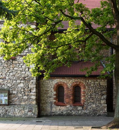 Zdjęcie nr 42: Kościół murowany, orientowany, jednonawowy, trójprzęsłowy, z transeptem i jednoprzęsłowym, węższym i niższym prezbiterium zamkniętym trójbocznie. Między nawą a transeptem po obu stronach znajdują się kruchty, do prezbiterium od strony północnej dostawiona kruchta złożona z dwóch lokalności. Ściany są rozczłonkowane filarami, tworzącymi płytkie arkadowe wnęki. Między nawą a prezbiterium arkada tęczowa. Sklepienie krzyżowe na gurtach spływających na filary. Prezbiterium oświetlają wąskie, prostokątne okna zamknięte ostrołukowo, w nawie i w transepcie znajdują się prostokątne okna prostokątne zamknięte półkoliście, w ścianie frontowej w dolnej części okna prostokątne zamknięte półkoliście, a w górnej podwójne okna prostokątne. Fasada ujęta dwiema narożnymi szkarpami, zwieńczona trójkątnie. Do niej dostawiona kruchta z dwuspadowym daszkiem i wejściem w kształcie prostokąta zamkniętego półkoliście. W kamiennej fasadzie znajdują się dołem okna prostokątne, zamknięte półkoliście, a górą  prostokątne, biforialne okna z nadprożem łukowatym wykonanym z cegły. Szczyt ceglany, podzielony na trzy strefy kamiennym wątkiem, z pięcioma wnękami prostokątnymi, zamkniętymi półkoliście, z wąskimi otworami w dolnej strefie i z owalnym oknem w drugiej. Elewacje boczne nawy ujęte skarpami. Dachy dwuspadowe, kryte dachówką, z wieżyczką na sygnaturkę.         