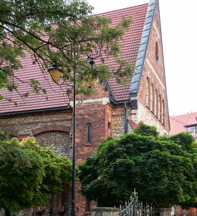 Zdjęcie nr 45: Kościół murowany, orientowany, jednonawowy, trójprzęsłowy, z transeptem i jednoprzęsłowym, węższym i niższym prezbiterium zamkniętym trójbocznie. Między nawą a transeptem po obu stronach znajdują się kruchty, do prezbiterium od strony północnej dostawiona kruchta złożona z dwóch lokalności. Ściany są rozczłonkowane filarami, tworzącymi płytkie arkadowe wnęki. Między nawą a prezbiterium arkada tęczowa. Sklepienie krzyżowe na gurtach spływających na filary. Prezbiterium oświetlają wąskie, prostokątne okna zamknięte ostrołukowo, w nawie i w transepcie znajdują się prostokątne okna prostokątne zamknięte półkoliście, w ścianie frontowej w dolnej części okna prostokątne zamknięte półkoliście, a w górnej podwójne okna prostokątne. Fasada ujęta dwiema narożnymi szkarpami, zwieńczona trójkątnie. Do niej dostawiona kruchta z dwuspadowym daszkiem i wejściem w kształcie prostokąta zamkniętego półkoliście. W kamiennej fasadzie znajdują się dołem okna prostokątne, zamknięte półkoliście, a górą  prostokątne, biforialne okna z nadprożem łukowatym wykonanym z cegły. Szczyt ceglany, podzielony na trzy strefy kamiennym wątkiem, z pięcioma wnękami prostokątnymi, zamkniętymi półkoliście, z wąskimi otworami w dolnej strefie i z owalnym oknem w drugiej. Elewacje boczne nawy ujęte skarpami. Dachy dwuspadowe, kryte dachówką, z wieżyczką na sygnaturkę.         