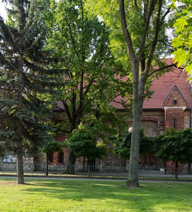 Zdjęcie nr 48: Kościół murowany, orientowany, jednonawowy, trójprzęsłowy, z transeptem i jednoprzęsłowym, węższym i niższym prezbiterium zamkniętym trójbocznie. Między nawą a transeptem po obu stronach znajdują się kruchty, do prezbiterium od strony północnej dostawiona kruchta złożona z dwóch lokalności. Ściany są rozczłonkowane filarami, tworzącymi płytkie arkadowe wnęki. Między nawą a prezbiterium arkada tęczowa. Sklepienie krzyżowe na gurtach spływających na filary. Prezbiterium oświetlają wąskie, prostokątne okna zamknięte ostrołukowo, w nawie i w transepcie znajdują się prostokątne okna prostokątne zamknięte półkoliście, w ścianie frontowej w dolnej części okna prostokątne zamknięte półkoliście, a w górnej podwójne okna prostokątne. Fasada ujęta dwiema narożnymi szkarpami, zwieńczona trójkątnie. Do niej dostawiona kruchta z dwuspadowym daszkiem i wejściem w kształcie prostokąta zamkniętego półkoliście. W kamiennej fasadzie znajdują się dołem okna prostokątne, zamknięte półkoliście, a górą  prostokątne, biforialne okna z nadprożem łukowatym wykonanym z cegły. Szczyt ceglany, podzielony na trzy strefy kamiennym wątkiem, z pięcioma wnękami prostokątnymi, zamkniętymi półkoliście, z wąskimi otworami w dolnej strefie i z owalnym oknem w drugiej. Elewacje boczne nawy ujęte skarpami. Dachy dwuspadowe, kryte dachówką, z wieżyczką na sygnaturkę.         