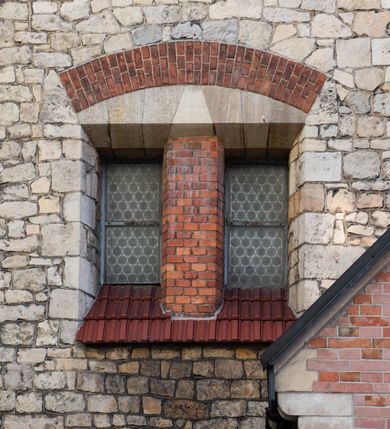 Zdjęcie nr 52: Kościół murowany, orientowany, jednonawowy, trójprzęsłowy, z transeptem i jednoprzęsłowym, węższym i niższym prezbiterium zamkniętym trójbocznie. Między nawą a transeptem po obu stronach znajdują się kruchty, do prezbiterium od strony północnej dostawiona kruchta złożona z dwóch lokalności. Ściany są rozczłonkowane filarami, tworzącymi płytkie arkadowe wnęki. Między nawą a prezbiterium arkada tęczowa. Sklepienie krzyżowe na gurtach spływających na filary. Prezbiterium oświetlają wąskie, prostokątne okna zamknięte ostrołukowo, w nawie i w transepcie znajdują się prostokątne okna prostokątne zamknięte półkoliście, w ścianie frontowej w dolnej części okna prostokątne zamknięte półkoliście, a w górnej podwójne okna prostokątne. Fasada ujęta dwiema narożnymi szkarpami, zwieńczona trójkątnie. Do niej dostawiona kruchta z dwuspadowym daszkiem i wejściem w kształcie prostokąta zamkniętego półkoliście. W kamiennej fasadzie znajdują się dołem okna prostokątne, zamknięte półkoliście, a górą  prostokątne, biforialne okna z nadprożem łukowatym wykonanym z cegły. Szczyt ceglany, podzielony na trzy strefy kamiennym wątkiem, z pięcioma wnękami prostokątnymi, zamkniętymi półkoliście, z wąskimi otworami w dolnej strefie i z owalnym oknem w drugiej. Elewacje boczne nawy ujęte skarpami. Dachy dwuspadowe, kryte dachówką, z wieżyczką na sygnaturkę.         