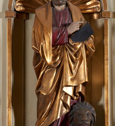 Zdjęcie nr 5: Ambona nadwieszona, przyścienna. Jej kosz jest ośmioboczny, wsparty na szerokich wolutach z plintą w kształcie winnego grona. Ścianki kosza podzielone kompozytowymi półkolumnami wspartymi na konsolkach z liściastymi wolutami. Między kolumienkami nisze konchowe z muszlami, wewnątrz których postacie ewangelistów, od lewej Mateusza, Marka, Łukasza i Jana. Figury ewangelistów ujęte całopostaciowo w pozycji stojącej, ubrane w długie tuniki i płaszcze. W dłoniach podtrzymują otwarte księgi, a u stóp widnieją ich symbole. Kosz wieńczy belkowanie wyłamujące się ponad kolumienkami, z fryzem zdobionym wiciami akantu. Zaplecek z dwiema płycinami zamkniętymi łukiem półkolistym. Ponad nimi pole w kształcie leżącego prostokąta, wewnątrz którego krzyż. Zaplecek flankowany dwiema listwami ujętymi ulistnionymi konsolami. Pośrodku dwie płyciny w kształcie wąskich prostokątów zakończonych półkoliście. W górnej części prostokątne pole w złoconym profilu z listkami wypełniającymi górne naroża, z przerwanym, wolutowym przyczółkiem i krzyżem o ramionach zakończonych trójlistnie. Baldachim na rzucie ośmioboku, z podwieszonym lambrekinem z chwostami i z ażurową koronką w kształcie wici roślinnej. Na baldachimie ośmioboczny cokół uskokowy, z płycinami w kształcie stojących prostokątów zamkniętych łukiem półkolistym nadwieszonym. Na cokole pełnoplastyczna figura stojącego Jana Chrzciciela, ubranego w wielbłądzią skórę i złocony płaszcz przerzucony przez lewe ramię. Jego twarz jest pociągła, okolona zarostem, włosy sięgające uszu. Prawą rękę unosi w geście błogosławieństwa, a w lewej trzyma krzyż z banderolą. W podniebiu gołębica Ducha Świętego na tle glorii promienistej. Ambona polichromowana na szaro, detale złocone. 
