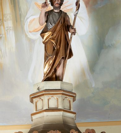 Zdjęcie nr 4: Ambona nadwieszona, przyścienna. Jej kosz jest ośmioboczny, wsparty na szerokich wolutach z plintą w kształcie winnego grona. Ścianki kosza podzielone kompozytowymi półkolumnami wspartymi na konsolkach z liściastymi wolutami. Między kolumienkami nisze konchowe z muszlami, wewnątrz których postacie ewangelistów, od lewej Mateusza, Marka, Łukasza i Jana. Figury ewangelistów ujęte całopostaciowo w pozycji stojącej, ubrane w długie tuniki i płaszcze. W dłoniach podtrzymują otwarte księgi, a u stóp widnieją ich symbole. Kosz wieńczy belkowanie wyłamujące się ponad kolumienkami, z fryzem zdobionym wiciami akantu. Zaplecek z dwiema płycinami zamkniętymi łukiem półkolistym. Ponad nimi pole w kształcie leżącego prostokąta, wewnątrz którego krzyż. Zaplecek flankowany dwiema listwami ujętymi ulistnionymi konsolami. Pośrodku dwie płyciny w kształcie wąskich prostokątów zakończonych półkoliście. W górnej części prostokątne pole w złoconym profilu z listkami wypełniającymi górne naroża, z przerwanym, wolutowym przyczółkiem i krzyżem o ramionach zakończonych trójlistnie. Baldachim na rzucie ośmioboku, z podwieszonym lambrekinem z chwostami i z ażurową koronką w kształcie wici roślinnej. Na baldachimie ośmioboczny cokół uskokowy, z płycinami w kształcie stojących prostokątów zamkniętych łukiem półkolistym nadwieszonym. Na cokole pełnoplastyczna figura stojącego Jana Chrzciciela, ubranego w wielbłądzią skórę i złocony płaszcz przerzucony przez lewe ramię. Jego twarz jest pociągła, okolona zarostem, włosy sięgające uszu. Prawą rękę unosi w geście błogosławieństwa, a w lewej trzyma krzyż z banderolą. W podniebiu gołębica Ducha Świętego na tle glorii promienistej. Ambona polichromowana na szaro, detale złocone. 
