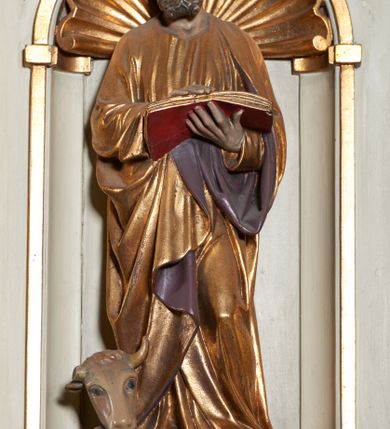 Zdjęcie nr 7: Ambona nadwieszona, przyścienna. Jej kosz jest ośmioboczny, wsparty na szerokich wolutach z plintą w kształcie winnego grona. Ścianki kosza podzielone kompozytowymi półkolumnami wspartymi na konsolkach z liściastymi wolutami. Między kolumienkami nisze konchowe z muszlami, wewnątrz których postacie ewangelistów, od lewej Mateusza, Marka, Łukasza i Jana. Figury ewangelistów ujęte całopostaciowo w pozycji stojącej, ubrane w długie tuniki i płaszcze. W dłoniach podtrzymują otwarte księgi, a u stóp widnieją ich symbole. Kosz wieńczy belkowanie wyłamujące się ponad kolumienkami, z fryzem zdobionym wiciami akantu. Zaplecek z dwiema płycinami zamkniętymi łukiem półkolistym. Ponad nimi pole w kształcie leżącego prostokąta, wewnątrz którego krzyż. Zaplecek flankowany dwiema listwami ujętymi ulistnionymi konsolami. Pośrodku dwie płyciny w kształcie wąskich prostokątów zakończonych półkoliście. W górnej części prostokątne pole w złoconym profilu z listkami wypełniającymi górne naroża, z przerwanym, wolutowym przyczółkiem i krzyżem o ramionach zakończonych trójlistnie. Baldachim na rzucie ośmioboku, z podwieszonym lambrekinem z chwostami i z ażurową koronką w kształcie wici roślinnej. Na baldachimie ośmioboczny cokół uskokowy, z płycinami w kształcie stojących prostokątów zamkniętych łukiem półkolistym nadwieszonym. Na cokole pełnoplastyczna figura stojącego Jana Chrzciciela, ubranego w wielbłądzią skórę i złocony płaszcz przerzucony przez lewe ramię. Jego twarz jest pociągła, okolona zarostem, włosy sięgające uszu. Prawą rękę unosi w geście błogosławieństwa, a w lewej trzyma krzyż z banderolą. W podniebiu gołębica Ducha Świętego na tle glorii promienistej. Ambona polichromowana na szaro, detale złocone. 
