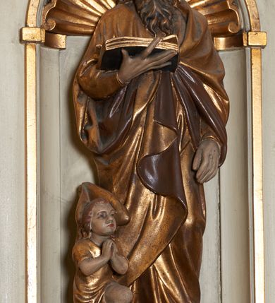 Zdjęcie nr 6: Ambona nadwieszona, przyścienna. Jej kosz jest ośmioboczny, wsparty na szerokich wolutach z plintą w kształcie winnego grona. Ścianki kosza podzielone kompozytowymi półkolumnami wspartymi na konsolkach z liściastymi wolutami. Między kolumienkami nisze konchowe z muszlami, wewnątrz których postacie ewangelistów, od lewej Mateusza, Marka, Łukasza i Jana. Figury ewangelistów ujęte całopostaciowo w pozycji stojącej, ubrane w długie tuniki i płaszcze. W dłoniach podtrzymują otwarte księgi, a u stóp widnieją ich symbole. Kosz wieńczy belkowanie wyłamujące się ponad kolumienkami, z fryzem zdobionym wiciami akantu. Zaplecek z dwiema płycinami zamkniętymi łukiem półkolistym. Ponad nimi pole w kształcie leżącego prostokąta, wewnątrz którego krzyż. Zaplecek flankowany dwiema listwami ujętymi ulistnionymi konsolami. Pośrodku dwie płyciny w kształcie wąskich prostokątów zakończonych półkoliście. W górnej części prostokątne pole w złoconym profilu z listkami wypełniającymi górne naroża, z przerwanym, wolutowym przyczółkiem i krzyżem o ramionach zakończonych trójlistnie. Baldachim na rzucie ośmioboku, z podwieszonym lambrekinem z chwostami i z ażurową koronką w kształcie wici roślinnej. Na baldachimie ośmioboczny cokół uskokowy, z płycinami w kształcie stojących prostokątów zamkniętych łukiem półkolistym nadwieszonym. Na cokole pełnoplastyczna figura stojącego Jana Chrzciciela, ubranego w wielbłądzią skórę i złocony płaszcz przerzucony przez lewe ramię. Jego twarz jest pociągła, okolona zarostem, włosy sięgające uszu. Prawą rękę unosi w geście błogosławieństwa, a w lewej trzyma krzyż z banderolą. W podniebiu gołębica Ducha Świętego na tle glorii promienistej. Ambona polichromowana na szaro, detale złocone. 
