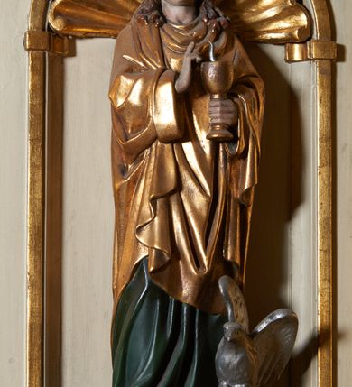 Zdjęcie nr 8: Ambona nadwieszona, przyścienna. Jej kosz jest ośmioboczny, wsparty na szerokich wolutach z plintą w kształcie winnego grona. Ścianki kosza podzielone kompozytowymi półkolumnami wspartymi na konsolkach z liściastymi wolutami. Między kolumienkami nisze konchowe z muszlami, wewnątrz których postacie ewangelistów, od lewej Mateusza, Marka, Łukasza i Jana. Figury ewangelistów ujęte całopostaciowo w pozycji stojącej, ubrane w długie tuniki i płaszcze. W dłoniach podtrzymują otwarte księgi, a u stóp widnieją ich symbole. Kosz wieńczy belkowanie wyłamujące się ponad kolumienkami, z fryzem zdobionym wiciami akantu. Zaplecek z dwiema płycinami zamkniętymi łukiem półkolistym. Ponad nimi pole w kształcie leżącego prostokąta, wewnątrz którego krzyż. Zaplecek flankowany dwiema listwami ujętymi ulistnionymi konsolami. Pośrodku dwie płyciny w kształcie wąskich prostokątów zakończonych półkoliście. W górnej części prostokątne pole w złoconym profilu z listkami wypełniającymi górne naroża, z przerwanym, wolutowym przyczółkiem i krzyżem o ramionach zakończonych trójlistnie. Baldachim na rzucie ośmioboku, z podwieszonym lambrekinem z chwostami i z ażurową koronką w kształcie wici roślinnej. Na baldachimie ośmioboczny cokół uskokowy, z płycinami w kształcie stojących prostokątów zamkniętych łukiem półkolistym nadwieszonym. Na cokole pełnoplastyczna figura stojącego Jana Chrzciciela, ubranego w wielbłądzią skórę i złocony płaszcz przerzucony przez lewe ramię. Jego twarz jest pociągła, okolona zarostem, włosy sięgające uszu. Prawą rękę unosi w geście błogosławieństwa, a w lewej trzyma krzyż z banderolą. W podniebiu gołębica Ducha Świętego na tle glorii promienistej. Ambona polichromowana na szaro, detale złocone. 
