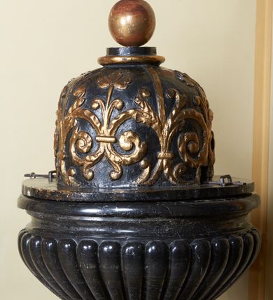 Zdjęcie nr 2: Chrzcielnica osadzona na okrągłej podstawie i prostopadłościennym, spłaszczonym cokole oraz cylindrycznym w przekroju trzonie, dołem lekko wybrzuszonym. Czara półkulista, puklowana, z profilowanym wylewem. Pokrywa drewniana, na okrągłej podstawie, cylindryczna, zaoblona u góry, zwieńczona wałkiem i kulą z krzyżem. Jej powierzchnia jest pokryta biegnącymi wzdłuż, złoconymi czterema taśmami i odchodzącymi od nich wolutowymi, spiętymi ze sobą gałązkami. 