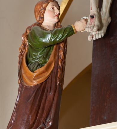 Zdjęcie nr 13: Grupa Ukrzyżowania złożona z ukrzyżowanego Chrystusa w typie christo vivo, stojących postaci Matki Boskiej i św. Jana oraz klęczącej Marii Magdaleny. Figura Chrystusa jest rzeźbą pełnoplastyczną, nieznacznie ściętą z tyłu, pozostałe są ścięte i wydrążone od tyłu. Zbawiciel przybity trzema gwoździami, z niemal prosto rozpostartymi rękami, z głową przechyloną na prawe ramię. Jego twarz jest pociągła, nos długi, oczy otwarte, twarz okolona kręconą, brązową brodą na głowie kręcone, sięgające szyi włosy i korona cierniowa pomalowana na zielono. Ręce z wyłamanymi barkami, z uwidocznionymi ścięgnami, klatka piersiowa wybrzuszona, z widocznymi żebrami i mostkiem, nogi smukłe z wyeksponowanymi kośćmi i mięśniami. Złocone perizonium przepasane podwójnym sznurem, z dwiema swobodnie rozwianymi połami po obu stronach bioder. Na naturalistycznie oddanym ciele zaznaczone strużki krwi. Na górnej belce titulus z literami: INRI". 
Matka Boska przedstawiona w pozycji stojącej, w kontrapoście, z rękami skrzyżowanymi na piersi. Głowę zwraca w kierunku Chrystusa, jej twarz jest owalna, włosy długie, brązowe, opadające na ramiona. Ubrana jest w czerwoną suknię z żółtą lamówką na rękawach, niebieski płaszcz o żółtym podbiciu i białą, długą chustę na głowie.    
Święty Jan ukazany w pozycji stojącej, w kontrapoście, z rękami złożonymi w geście modlitwy. Jego twarz jest owalna, oczy szeroko otwarte, włosy brązowe, kręcone, opadające na ramiona. Apostoł jest ubrany w zieloną tunikę i czerwony płaszcz z pomarańczowym podbiciem, przewieszony przez lewe ramię i ugiętą rękę. 
Po prawej stronie krzyża klęczy Maria Magdalena, ukazana prawym profilem, z prawą ręką, w której trzyma gąbkę wyciągniętą ku krzyżowi. Jej twarz jest pociągła z prostym nosem, włosy jasnobrązowe, długie, kręcone, opadające na plecy. Jest ubrana w zieloną tunikę i brązowy płaszcz o jaśniejszym podbiciu, opadający z lewego ramienia.
Na belce w kolorze czerwonym złocony napis: "Benedictus XVI SPE SALVI FACTI SUMUS A(NNO) D(OMINI) MMVII".
