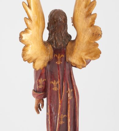 Zdjęcie nr 2: Pełnoplastyczna rzeźba stojącego w kontrapoście na chmurach anioła, z głową zwróconą w lewo, z prawą ręką, ugiętą w łokciu, wzniesioną wzwyż, lewą opuszczoną wzdłuż ciała. Twarz o rysach młodzieńca z prostym nosem, różowymi ustami, niebieskimi oczami, okolona włosami opadającymi w lokach na plecy. Anioł ubrany w długą czerwoną tunikę z szerokimi rękawami, malowaną w złote lilie herbowe. Strzeliste skrzydła rozpostarte, malowane na złoto. 