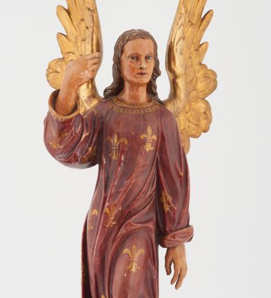 Zdjęcie nr 1: Pełnoplastyczna rzeźba stojącego w kontrapoście na chmurach anioła, z głową zwróconą w lewo, z prawą ręką, ugiętą w łokciu, wzniesioną wzwyż, lewą opuszczoną wzdłuż ciała. Twarz o rysach młodzieńca z prostym nosem, różowymi ustami, niebieskimi oczami, okolona włosami opadającymi w lokach na plecy. Anioł ubrany w długą czerwoną tunikę z szerokimi rękawami, malowaną w złote lilie herbowe. Strzeliste skrzydła rozpostarte, malowane na złoto. 