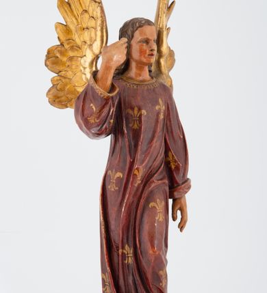 Zdjęcie nr 4: Pełnoplastyczna rzeźba stojącego w kontrapoście na chmurach anioła, z głową zwróconą w lewo, z prawą ręką, ugiętą w łokciu, wzniesioną wzwyż, lewą opuszczoną wzdłuż ciała. Twarz o rysach młodzieńca z prostym nosem, różowymi ustami, niebieskimi oczami, okolona włosami opadającymi w lokach na plecy. Anioł ubrany w długą czerwoną tunikę z szerokimi rękawami, malowaną w złote lilie herbowe. Strzeliste skrzydła rozpostarte, malowane na złoto. 