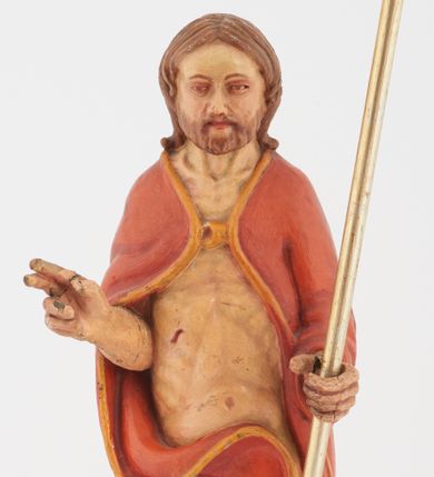 Zdjęcie nr 1: Pełnoplastyczna rzeźba Chrystusa Zmartwychwstałego stojącego na chmurze z prawą ręką wzniesioną w geście błogosławieństwa, lewą trzymającego krzyż na długim drzewcu. Twarz szeroka, z wydatnym nosem, ciemnobrązowymi oczami, ciemnoróżowymi ustami, okolona zarostem oraz włosami z przedziałkiem pośrodku głowy, opadającymi na plecy. Karnacja jasnobeżowa. Chrystus ukazany nagi, przesłonięty czerwonym płaszczem, spiętym na piersi, opadającym ukośnymi fałdami do ziemi. 