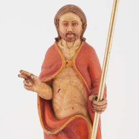 Zdjęcie nr 1: Pełnoplastyczna rzeźba Chrystusa Zmartwychwstałego stojącego na chmurze z prawą ręką wzniesioną w geście błogosławieństwa, lewą trzymającego krzyż na długim drzewcu. Twarz szeroka, z wydatnym nosem, ciemnobrązowymi oczami, ciemnoróżowymi ustami, okolona zarostem oraz włosami z przedziałkiem pośrodku głowy, opadającymi na plecy. Karnacja jasnobeżowa. Chrystus ukazany nagi, przesłonięty czerwonym płaszczem, spiętym na piersi, opadającym ukośnymi fałdami do ziemi. 