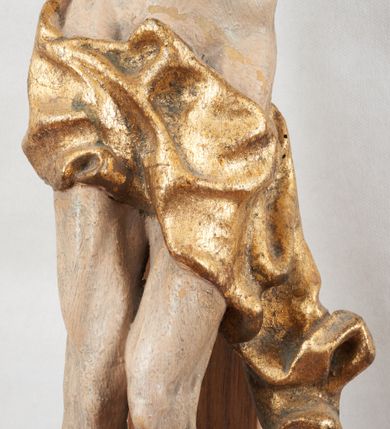 Zdjęcie nr 3: Figura pełnoplastyczna, lekko obcięta z tyłu. Rzeźba ukazuje Chrystusa przybitego do krzyża trzema gwoździami, w silnym zwisie, o subtelnie zarysowanej esowato sylwetce. Jego twarz jest modelowana sumarycznie, a rysy zatarte nadmierną ilością farby, z zaznaczoną czarną brodą, włosami opadającymi na kark i prawe ramię oraz złoconą koroną cierniową. Ciało jest smukłe, delikatnie kształtowane, z lekko zaznaczonym mostkiem i żebrami, z miękko układającym się perizonium o ekspresyjnie zawiniętym i luźno wijącym się brzegu. Na górnej belce krzyża titulus z napisem: „IN/RI”. 