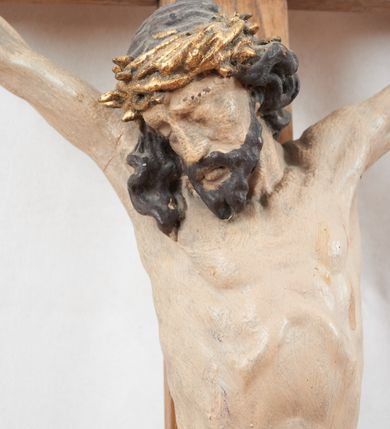 Zdjęcie nr 2: Figura pełnoplastyczna, lekko obcięta z tyłu. Rzeźba ukazuje Chrystusa przybitego do krzyża trzema gwoździami, w silnym zwisie, o subtelnie zarysowanej esowato sylwetce. Jego twarz jest modelowana sumarycznie, a rysy zatarte nadmierną ilością farby, z zaznaczoną czarną brodą, włosami opadającymi na kark i prawe ramię oraz złoconą koroną cierniową. Ciało jest smukłe, delikatnie kształtowane, z lekko zaznaczonym mostkiem i żebrami, z miękko układającym się perizonium o ekspresyjnie zawiniętym i luźno wijącym się brzegu. Na górnej belce krzyża titulus z napisem: „IN/RI”. 