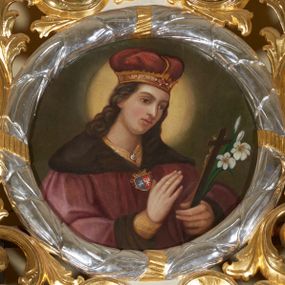 Zdjęcie nr 1: Obraz okrągły, ujęty srebrzoną i złoconą ramą w formie wieńca laurowego oraz szerokim, ażurowym obramieniem utworzonym z suchego akantu. Święty Kazimierz ujęty półpostaciowo, w trzech czwartych zwrócony w lewo, z głową lekko pochyloną w dół. Jego twarz jest pociągła o delikatnych, młodzieńczych rysach, włosy długie, kręcone, ciemnobrązowe, opadające na plecy i ramiona. Ubrany w ciemoczerwony płaszcz książęcy, spod którego pod szyją wystaje fragment żółtego kaftana, a na rękach – rękawy; na głowie nosi mitrę książęcą. Płaszcz jest ciemnoczerwony, ma szeroki futrzany kołnierz i mankiety. Spięty jest na piersiach złotą zapinką z herbami Jagiellonów – Pogonią i Orłem. W lewej dłoni święty trzyma krucyfiks i białą lilię, a prawą unosi na wysokości klatki piersiowej. Wokół jego głowy świetlisty nimb. Tło jednolite, ciemnobrązowe. Kolorystyka o stonowanym nasyceniu, przyciemniona. 

