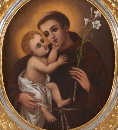 Zdjęcie nr 1: Obraz ujęty ramą w kształcie stojącego prostokąta z wycięciem w kształcie stojącego owalu, profilowaną, zdobioną motywami roślinno-kwiatowymi w narożach oraz wicią suchego akantu. Święty Antoni ujęty półpostaciowo, w trzech czwartych zwrócony w prawo. Jego twarz jest owalna o delikatnych, młodzieńczych rysach. Włosy ma krótkie, ciemnobrązowe, z wyciętą tonsurą. Święty jest ubrany w brązowy habit franciszkański. W lewej dłoni trzyma białą lilię, prawą podtrzymuje Dzieciątko Jezus. Trzymany na ręku Jezus ukazany w pozycji siedzącej, w trzech czwartych, zwrócony w lewo. Jego głowa jest odchylona do tyłu, wzrok skierowany w stronę twarzy świętego. Twarz ma owalną o delikatnych rysach, włosy jasnobrązowe, krótkie i falowane. Jego biodra i częściowo nóżki przesłania biała pielucha. Lewą rączkę wspiera na podbródku świętego, prawą unosi na wysokości klatki piersiowej. Tło nieokreślone, brązowe, rozświetlone nimbami wokół głów postaci. Kolorystyka w ciepłej tonacji, nasycona, o delikatnym modelunku.  
