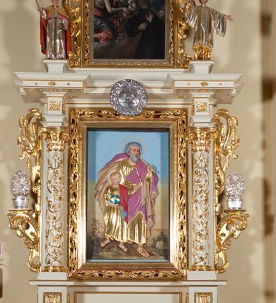 Zdjęcie nr 2: Ołtarz architektoniczny, jednokondygnacyjny, jednoosiowy, ze zwieńczeniem. Jego mensa i antepedium są drewniane. Antepedium w kształcie leżącego prostokąta zostało ujęte profilowaną, złoconą ramą, a wypełnione dekoracją malarską z motywem krzyża i białych lilii pośrodku, ujętych ornamentalną bordiurą ze stylizowanych motywów roślinno-kwiatowych. Retabulum jest osadzone na niewysokim cokole i ujęte kolumnami korynckimi, dźwigającymi wyłamujące się ponad nimi, przerwane w partii architrawu i fryzu belkowanie z silnie wysuniętym gzymsem. Do kolumn dostawione po bokach ażurowe uszaki formowane z ornamentu małżowinowo-chrząstkowego, z parą wazonów z kwiatami w połowie wysokości. Trzony kolumn są pokryte płaskorzeźbionymi gałązkami winorośli. W partiach fryzu belkowania widnieje motyw rozetek; na cokołach ornamenty małżowinowe. Gzyms zdobiony drobną ornamentyką roślinną, pośrodku kolista gloria z Okiem Opatrzności. Zwieńczenie na niewysokim cokole o zryzalitowanych bokach, w kształcie stojącego prostokąta o wciętych górnych narożach. Nad nim szczyt w formie owalnego kartusza o fantazyjnym wykroju. Zwieńczenie jest ujęte parą ażurowych uszaków w formie ornamentu małżowinowo–chrząstkowego. Pole środkowe retabulum w kształcie stojącego prostokąta, ujętego profilowaną, złoconą ramą zdobioną ażurową ornamentyką małżowinowo-chrząstkową. Wewnątrz płaskorzeźba ukazująca św. Józefa z Jezusem. Pole zwieńczenia w kształcie stojącego prostokąta zamkniętego nadwieszonym łukiem, ujęte profilowaną, złoconą ramą z ażurową ornamentyką małżowinowo-chrząstkową. W nim obraz „Komunia św. Stanisława Kostki”. Pole szczytu w kształcie leżącego owalu z obrazem Matki Boskiej Częstochowskiej. Zwieńczenie jest flankowane ustawionymi na zryzalitowanych cokołach figurami św. Stanisława biskupa i św. Jacka (?). Struktura polichromowana w kolorze jasnego beżu. Ornamentyka i partie detalu architektonicznego złocone i srebrzone. 

