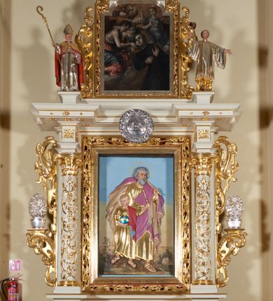 Zdjęcie nr 1: Ołtarz architektoniczny, jednokondygnacyjny, jednoosiowy, ze zwieńczeniem. Jego mensa i antepedium są drewniane. Antepedium w kształcie leżącego prostokąta zostało ujęte profilowaną, złoconą ramą, a wypełnione dekoracją malarską z motywem krzyża i białych lilii pośrodku, ujętych ornamentalną bordiurą ze stylizowanych motywów roślinno-kwiatowych. Retabulum jest osadzone na niewysokim cokole i ujęte kolumnami korynckimi, dźwigającymi wyłamujące się ponad nimi, przerwane w partii architrawu i fryzu belkowanie z silnie wysuniętym gzymsem. Do kolumn dostawione po bokach ażurowe uszaki formowane z ornamentu małżowinowo-chrząstkowego, z parą wazonów z kwiatami w połowie wysokości. Trzony kolumn są pokryte płaskorzeźbionymi gałązkami winorośli. W partiach fryzu belkowania widnieje motyw rozetek; na cokołach ornamenty małżowinowe. Gzyms zdobiony drobną ornamentyką roślinną, pośrodku kolista gloria z Okiem Opatrzności. Zwieńczenie na niewysokim cokole o zryzalitowanych bokach, w kształcie stojącego prostokąta o wciętych górnych narożach. Nad nim szczyt w formie owalnego kartusza o fantazyjnym wykroju. Zwieńczenie jest ujęte parą ażurowych uszaków w formie ornamentu małżowinowo–chrząstkowego. Pole środkowe retabulum w kształcie stojącego prostokąta, ujętego profilowaną, złoconą ramą zdobioną ażurową ornamentyką małżowinowo-chrząstkową. Wewnątrz płaskorzeźba ukazująca św. Józefa z Jezusem. Pole zwieńczenia w kształcie stojącego prostokąta zamkniętego nadwieszonym łukiem, ujęte profilowaną, złoconą ramą z ażurową ornamentyką małżowinowo-chrząstkową. W nim obraz „Komunia św. Stanisława Kostki”. Pole szczytu w kształcie leżącego owalu z obrazem Matki Boskiej Częstochowskiej. Zwieńczenie jest flankowane ustawionymi na zryzalitowanych cokołach figurami św. Stanisława biskupa i św. Jacka (?). Struktura polichromowana w kolorze jasnego beżu. Ornamentyka i partie detalu architektonicznego złocone i srebrzone. 
