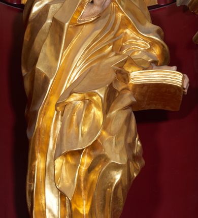 Zdjęcie nr 2: Święty Joachim został ukazany frontalnie, całopostaciowo, w lekkim kontrapoście, z prawą ręką wyciągniętą na piersi w geście błogosławieństwa, a lewą przytrzymującą księgę wspartą na biodrze. Jest ubrany w długą suknię i płaszcz spięty na piersi, okrywający plecy i przerzucony przez lewą nogę. Twarz o wydatnych policzkach, z głębokimi oczodołami, masywnym nosie i otwartymi ustami. Włosy krótkie, kręcone, układane w pojedyncze pukle; broda jest krótka, falująca.  
