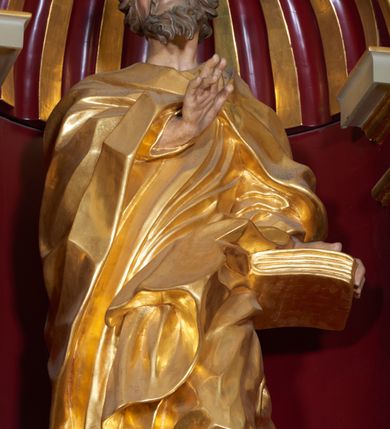 Zdjęcie nr 4: Święty Joachim został ukazany frontalnie, całopostaciowo, w lekkim kontrapoście, z prawą ręką wyciągniętą na piersi w geście błogosławieństwa, a lewą przytrzymującą księgę wspartą na biodrze. Jest ubrany w długą suknię i płaszcz spięty na piersi, okrywający plecy i przerzucony przez lewą nogę. Twarz o wydatnych policzkach, z głębokimi oczodołami, masywnym nosie i otwartymi ustami. Włosy krótkie, kręcone, układane w pojedyncze pukle; broda jest krótka, falująca.  
