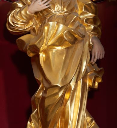 Zdjęcie nr 2: Święta Anna została ukazana frontalnie, całopostaciowo, w lekkim kontrapoście, z prawą ręką zgiętą w łokciu i uniesioną na wysokości piersi, a lewą opuszczoną wzdłuż ciała. Ubrana w długą suknię przewiązaną, płaszcz zarzucony na plecy i welon na głowie. Ma twarz o ostrych rysach, z wydatnymi kościami policzkowymi, szerokim, dużym nosem, otwartymi oczami i zamkniętymi ustami. 