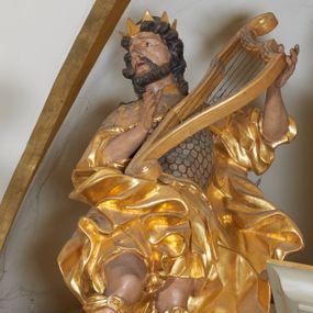 Zdjęcie nr 1: Figura całopostaciowa, zwrócona frontalnie, w kontrapoście, delikatnie przechylona w prawo, z harfą w rękach wspartą na biodrze. Król Dawid jest ubrany w zbroję łuskową, z krótkimi piórami i płaszcz narzucony na ramiona, opadający na plecy z zawiniętym fragmentem na prawej nodze. Jego twarz jest owalna, nos niewielki, delikatnie zadarty, oczy małe, wpatrzone na wprost, brwi uniesione, usta pełne, rozchylone; okolona krótką brodą. Włosy krótkie, silnie skręcone w poszczególne pasma loków okalających twarz. Tkanina jego ubioru ekspresyjnie drapowana w płynne, miękkie fałdy, miejscami skręcona, z rozwianym fragmentem przy lewym boku. Na głowie Dawida korona otwarta. Pod kolanami zawiązane wstęgi, na stopach widoczne sandały. 