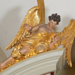 Zdjęcie nr 1: Para figur aniołów na przerwanym przyczółku w układzie przeciwstawnym. Ukazane w pozycji siedzącej, z podkurczoną prawą i wyciągniętymi wzdłuż przyczółka nogami, z pochyloną głową i rozłożonymi rękami. Ich twarze są szczupłe, o wyrazistych rysach, otwartych oczach i ustach. Włosy krótkie, rzeźbione w pojedyncze silnie skręcone, ekspresyjne pukle. Anioły ubrane są w szaty przewiązane przez jedno ramię, odsłaniające tors i fragmenty nóg, modelowane obficie w liczne fałdy i marszczenia. Skrzydła duże, delikatnie rozłożone. Polichromia naturalistyczna w odsłoniętych partiach ciała, szaty i atrybuty złocone.
