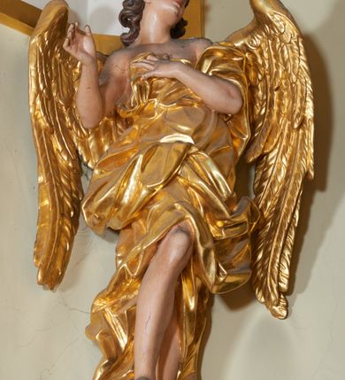 Zdjęcie nr 3: Figura zwrócona frontalnie, w wykroku, z wypchniętym lewym biodrem, obie ręce wyciągnięte w geście w przeciwną stronę, głowa skierowana w prawo, rzeźba w płynnym ruchu. Twarz owalna, o pełnych policzkach i delikatnych rysach. Nos niewielki, lekko zadarty, oczy małe wpatrzone na wprost, usta niewielki, pełne, rozchylone. Włosy krótkie, rzeźbione w pojedyncze, silnie skręcone pukle, ekspresyjnie rozwiane. Anioł jest ubrany w szatę sięgającą kolan, przewiązaną diagonalnie przez prawe ramię i oplatającą postać wokół z silnie drapowanym fragmentem zawijającym się na ramieniu oraz w partii nóg i marszczonym w obrębie torsu. Skrzydła duże, delikatnie rozchylone. Polichromia naturalistyczna w odsłoniętych partiach ciała, szaty złocone.

Figura drugiego anioła zwrócona frontalnie, w kontrapoście i wykroku, o esowato wygiętej sylwetce, głowa skierowana w lewo, delikatnie uniesiona. Lewa ręka złożona na piersi, prawa ugięta, wyciągnięta przed siebie w geście. Twarz owalna, młodzieńcza o delikatnych rysach, niewielki, lekko zadarty nos, oczy małe zwrócone ku górze, usta niewielkie o pełnych wargach. Włosy półdługie, głęboko rzeźbione w pojedyncze, wijące się pasma, ekspresyjnie poruszone, opadające na kark. Anioł jest ubrany w marszczoną tunikę, ściśle przylegającą do ciała, odsłaniającą tors i nogi oraz płaszcz przewiązany przez lewe ramię, z fragmentem podtrzymywanym dłonią na piersi, dalej otaczający postać, opadający na tył, z zawiniętą z przodu postaci partią materiału. Tkanina miękko rzeźbiona w grube, ekspresyjnie kształtowane fałdy, płynnie otaczająca postać z wywiniętym fragmentem na prawym boku. Skrzydła duże, złożone. Polichromia naturalistyczna w odsłoniętych partiach ciała, szaty i atrybuty złocone.
