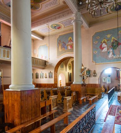 Zdjęcie nr 27: Kościół murowany z cegły na niskiej, kamiennej podmurówce, orientowany, jednonawowy ze zredukowanym transeptem oraz nieco niższym, zamkniętym półkoliście prezbiterium. Do północno-wschodniego narożnika nawy (przy prezbiterium) przylega założona na rzucie prostokąta, oszkarpowana zakrystia dostępna półkolistym portalem od strony północnej. Do południowo-wschodniego narożnika nawy dostawiona kaplica Matki Boskiej na rzucie prostokąta zamknięta od wschodu niewielką absydą. Ramiona transeptu zredukowane do roli prostokątnych kaplic. Do południowo-zachodniego i północno-zachodniego narożnika nawy dobudowane nowsze kruchty boczne założone na rzucie prostokąta dostępne portalami o półkolistym wykroju. Kruchta zachodnia na rzucie prostokąta dostępna nowym, prostokątnym wejściem. W ścianach północnej i południowej widoczne, zamurowane, starsze otwory wejściowe (od południa w miejsce portalu okrągłe okno). Dach nad nawą dwuspadowy z trzecią połacią zakrywającą ścianę szczytową; w części wschodniej wieloboczna wieżyczka na sygnaturkę z glorietą zwieńczoną krzyżem. Kruchty oraz kaplice boczne kryte dachami trójpołaciowymi, prezbiterium jednopołaciowym; nad zakrystią dach mansardowy z prostokątnym oknem w lukarnie. Pokrycia dachowe wykonane są z blachy (pierwotnie była to czerwona dachówka). W nawie i prezbiterium strop o konstrukcji żelbetowej wsparty na dziewięciu masywnych kolumnach ustawionych na wysokich cokołach; kaplice boczne sklepione krzyżowo, w zakrystii założony betonowy strop. Chór muzyczny murowany, wsparty na pierwszej od zachodu parze kolumn dźwigających strop. Fasada jednokondygnacyjna, trójosiowa z umieszczoną w osi centralnej prostopadłościenną kruchtą mieszczącą prostokątny otwór wejściowy (nowy). Okna w kształcie stojącego prostokąta o smukłych proporcjach, zamknięte półkoliście. Okno środkowe, umieszczone nieco wyżej, niższe od pozostałych. W ścianach zachodnich krucht bocznych po jednym niewielkim oknie o wykroju półkolistym. Trójkątna ściana szczytowa zasłonięta blaszanym dachem o przełamanej w dolnej części połaci, zwieńczona niewielkim, metalowym krzyżem. Elewacje boczne jednokondygnacyjne, o nieregularnym przebiegu osi. W elewacji południowej w pierwszej osi ceglany portal z nadświetlem o wykroju półkolistym, w drugiej okrągłe okno doświetlające kaplicę boczną, w kolejnych: półkolisty ceglany portal do zakrystii oraz okno o półkolistym wykroju z motywem biforium. W elewacji północnej w osi pierwszej i drugiej niewielkie półkoliście wykrojone okna, w osi trzeciej okrągłe okno doświetlające kaplicę, w osi czwartej natomiast ceglany portal  z nadświetlem o wykroju półkolistym. W prezbiterium cztery okna o wykroju półkolistym. W trzeciej osi, pomiędzy oknami, ujęta wielobocznymi filarami dźwigającymi, wydatny, profilowany gzyms tynkowana na biało nisza z figurą Matki Boskiej Fatimskiej umieszczonej pod baldachimem. Górną część murów nawy, prezbiterium, zakrystii, kaplic oraz obu krucht bocznych obiega profilowany gzyms okapowy. 