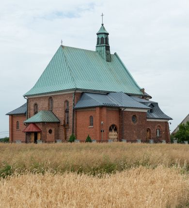 Zdjęcie nr 24: Kościół murowany z cegły na niskiej, kamiennej podmurówce, orientowany, jednonawowy ze zredukowanym transeptem oraz nieco niższym, zamkniętym półkoliście prezbiterium. Do północno-wschodniego narożnika nawy (przy prezbiterium) przylega założona na rzucie prostokąta, oszkarpowana zakrystia dostępna półkolistym portalem od strony północnej. Do południowo-wschodniego narożnika nawy dostawiona kaplica Matki Boskiej na rzucie prostokąta zamknięta od wschodu niewielką absydą. Ramiona transeptu zredukowane do roli prostokątnych kaplic. Do południowo-zachodniego i północno-zachodniego narożnika nawy dobudowane nowsze kruchty boczne założone na rzucie prostokąta dostępne portalami o półkolistym wykroju. Kruchta zachodnia na rzucie prostokąta dostępna nowym, prostokątnym wejściem. W ścianach północnej i południowej widoczne, zamurowane, starsze otwory wejściowe (od południa w miejsce portalu okrągłe okno). Dach nad nawą dwuspadowy z trzecią połacią zakrywającą ścianę szczytową; w części wschodniej wieloboczna wieżyczka na sygnaturkę z glorietą zwieńczoną krzyżem. Kruchty oraz kaplice boczne kryte dachami trójpołaciowymi, prezbiterium jednopołaciowym; nad zakrystią dach mansardowy z prostokątnym oknem w lukarnie. Pokrycia dachowe wykonane są z blachy (pierwotnie była to czerwona dachówka). W nawie i prezbiterium strop o konstrukcji żelbetowej wsparty na dziewięciu masywnych kolumnach ustawionych na wysokich cokołach; kaplice boczne sklepione krzyżowo, w zakrystii założony betonowy strop. Chór muzyczny murowany, wsparty na pierwszej od zachodu parze kolumn dźwigających strop. Fasada jednokondygnacyjna, trójosiowa z umieszczoną w osi centralnej prostopadłościenną kruchtą mieszczącą prostokątny otwór wejściowy (nowy). Okna w kształcie stojącego prostokąta o smukłych proporcjach, zamknięte półkoliście. Okno środkowe, umieszczone nieco wyżej, niższe od pozostałych. W ścianach zachodnich krucht bocznych po jednym niewielkim oknie o wykroju półkolistym. Trójkątna ściana szczytowa zasłonięta blaszanym dachem o przełamanej w dolnej części połaci, zwieńczona niewielkim, metalowym krzyżem. Elewacje boczne jednokondygnacyjne, o nieregularnym przebiegu osi. W elewacji południowej w pierwszej osi ceglany portal z nadświetlem o wykroju półkolistym, w drugiej okrągłe okno doświetlające kaplicę boczną, w kolejnych: półkolisty ceglany portal do zakrystii oraz okno o półkolistym wykroju z motywem biforium. W elewacji północnej w osi pierwszej i drugiej niewielkie półkoliście wykrojone okna, w osi trzeciej okrągłe okno doświetlające kaplicę, w osi czwartej natomiast ceglany portal  z nadświetlem o wykroju półkolistym. W prezbiterium cztery okna o wykroju półkolistym. W trzeciej osi, pomiędzy oknami, ujęta wielobocznymi filarami dźwigającymi, wydatny, profilowany gzyms tynkowana na biało nisza z figurą Matki Boskiej Fatimskiej umieszczonej pod baldachimem. Górną część murów nawy, prezbiterium, zakrystii, kaplic oraz obu krucht bocznych obiega profilowany gzyms okapowy. 