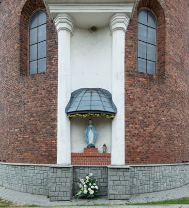 Zdjęcie nr 10: Kościół murowany z cegły na niskiej, kamiennej podmurówce, orientowany, jednonawowy ze zredukowanym transeptem oraz nieco niższym, zamkniętym półkoliście prezbiterium. Do północno-wschodniego narożnika nawy (przy prezbiterium) przylega założona na rzucie prostokąta, oszkarpowana zakrystia dostępna półkolistym portalem od strony północnej. Do południowo-wschodniego narożnika nawy dostawiona kaplica Matki Boskiej na rzucie prostokąta zamknięta od wschodu niewielką absydą. Ramiona transeptu zredukowane do roli prostokątnych kaplic. Do południowo-zachodniego i północno-zachodniego narożnika nawy dobudowane nowsze kruchty boczne założone na rzucie prostokąta dostępne portalami o półkolistym wykroju. Kruchta zachodnia na rzucie prostokąta dostępna nowym, prostokątnym wejściem. W ścianach północnej i południowej widoczne, zamurowane, starsze otwory wejściowe (od południa w miejsce portalu okrągłe okno). Dach nad nawą dwuspadowy z trzecią połacią zakrywającą ścianę szczytową; w części wschodniej wieloboczna wieżyczka na sygnaturkę z glorietą zwieńczoną krzyżem. Kruchty oraz kaplice boczne kryte dachami trójpołaciowymi, prezbiterium jednopołaciowym; nad zakrystią dach mansardowy z prostokątnym oknem w lukarnie. Pokrycia dachowe wykonane są z blachy (pierwotnie była to czerwona dachówka). W nawie i prezbiterium strop o konstrukcji żelbetowej wsparty na dziewięciu masywnych kolumnach ustawionych na wysokich cokołach; kaplice boczne sklepione krzyżowo, w zakrystii założony betonowy strop. Chór muzyczny murowany, wsparty na pierwszej od zachodu parze kolumn dźwigających strop. Fasada jednokondygnacyjna, trójosiowa z umieszczoną w osi centralnej prostopadłościenną kruchtą mieszczącą prostokątny otwór wejściowy (nowy). Okna w kształcie stojącego prostokąta o smukłych proporcjach, zamknięte półkoliście. Okno środkowe, umieszczone nieco wyżej, niższe od pozostałych. W ścianach zachodnich krucht bocznych po jednym niewielkim oknie o wykroju półkolistym. Trójkątna ściana szczytowa zasłonięta blaszanym dachem o przełamanej w dolnej części połaci, zwieńczona niewielkim, metalowym krzyżem. Elewacje boczne jednokondygnacyjne, o nieregularnym przebiegu osi. W elewacji południowej w pierwszej osi ceglany portal z nadświetlem o wykroju półkolistym, w drugiej okrągłe okno doświetlające kaplicę boczną, w kolejnych: półkolisty ceglany portal do zakrystii oraz okno o półkolistym wykroju z motywem biforium. W elewacji północnej w osi pierwszej i drugiej niewielkie półkoliście wykrojone okna, w osi trzeciej okrągłe okno doświetlające kaplicę, w osi czwartej natomiast ceglany portal  z nadświetlem o wykroju półkolistym. W prezbiterium cztery okna o wykroju półkolistym. W trzeciej osi, pomiędzy oknami, ujęta wielobocznymi filarami dźwigającymi, wydatny, profilowany gzyms tynkowana na biało nisza z figurą Matki Boskiej Fatimskiej umieszczonej pod baldachimem. Górną część murów nawy, prezbiterium, zakrystii, kaplic oraz obu krucht bocznych obiega profilowany gzyms okapowy. 