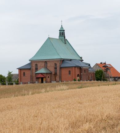Zdjęcie nr 2: Kościół murowany z cegły na niskiej, kamiennej podmurówce, orientowany, jednonawowy ze zredukowanym transeptem oraz nieco niższym, zamkniętym półkoliście prezbiterium. Do północno-wschodniego narożnika nawy (przy prezbiterium) przylega założona na rzucie prostokąta, oszkarpowana zakrystia dostępna półkolistym portalem od strony północnej. Do południowo-wschodniego narożnika nawy dostawiona kaplica Matki Boskiej na rzucie prostokąta zamknięta od wschodu niewielką absydą. Ramiona transeptu zredukowane do roli prostokątnych kaplic. Do południowo-zachodniego i północno-zachodniego narożnika nawy dobudowane nowsze kruchty boczne założone na rzucie prostokąta dostępne portalami o półkolistym wykroju. Kruchta zachodnia na rzucie prostokąta dostępna nowym, prostokątnym wejściem. W ścianach północnej i południowej widoczne, zamurowane, starsze otwory wejściowe (od południa w miejsce portalu okrągłe okno). Dach nad nawą dwuspadowy z trzecią połacią zakrywającą ścianę szczytową; w części wschodniej wieloboczna wieżyczka na sygnaturkę z glorietą zwieńczoną krzyżem. Kruchty oraz kaplice boczne kryte dachami trójpołaciowymi, prezbiterium jednopołaciowym; nad zakrystią dach mansardowy z prostokątnym oknem w lukarnie. Pokrycia dachowe wykonane są z blachy (pierwotnie była to czerwona dachówka). W nawie i prezbiterium strop o konstrukcji żelbetowej wsparty na dziewięciu masywnych kolumnach ustawionych na wysokich cokołach; kaplice boczne sklepione krzyżowo, w zakrystii założony betonowy strop. Chór muzyczny murowany, wsparty na pierwszej od zachodu parze kolumn dźwigających strop. Fasada jednokondygnacyjna, trójosiowa z umieszczoną w osi centralnej prostopadłościenną kruchtą mieszczącą prostokątny otwór wejściowy (nowy). Okna w kształcie stojącego prostokąta o smukłych proporcjach, zamknięte półkoliście. Okno środkowe, umieszczone nieco wyżej, niższe od pozostałych. W ścianach zachodnich krucht bocznych po jednym niewielkim oknie o wykroju półkolistym. Trójkątna ściana szczytowa zasłonięta blaszanym dachem o przełamanej w dolnej części połaci, zwieńczona niewielkim, metalowym krzyżem. Elewacje boczne jednokondygnacyjne, o nieregularnym przebiegu osi. W elewacji południowej w pierwszej osi ceglany portal z nadświetlem o wykroju półkolistym, w drugiej okrągłe okno doświetlające kaplicę boczną, w kolejnych: półkolisty ceglany portal do zakrystii oraz okno o półkolistym wykroju z motywem biforium. W elewacji północnej w osi pierwszej i drugiej niewielkie półkoliście wykrojone okna, w osi trzeciej okrągłe okno doświetlające kaplicę, w osi czwartej natomiast ceglany portal  z nadświetlem o wykroju półkolistym. W prezbiterium cztery okna o wykroju półkolistym. W trzeciej osi, pomiędzy oknami, ujęta wielobocznymi filarami dźwigającymi, wydatny, profilowany gzyms tynkowana na biało nisza z figurą Matki Boskiej Fatimskiej umieszczonej pod baldachimem. Górną część murów nawy, prezbiterium, zakrystii, kaplic oraz obu krucht bocznych obiega profilowany gzyms okapowy. 
